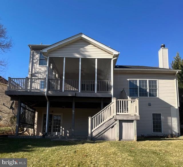 back of property with a deck, a sunroom, and a lawn