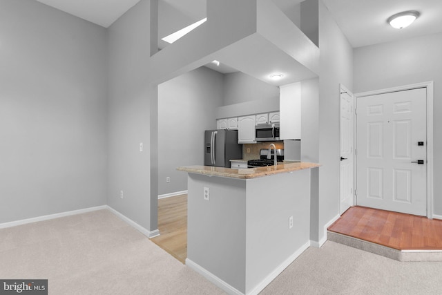 kitchen featuring appliances with stainless steel finishes, white cabinetry, tasteful backsplash, light carpet, and kitchen peninsula