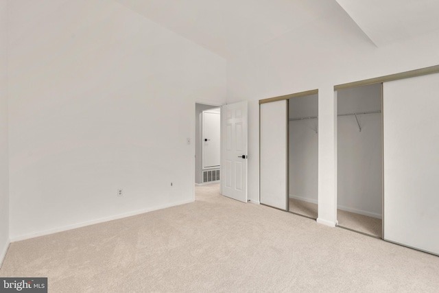 unfurnished bedroom with light colored carpet and two closets