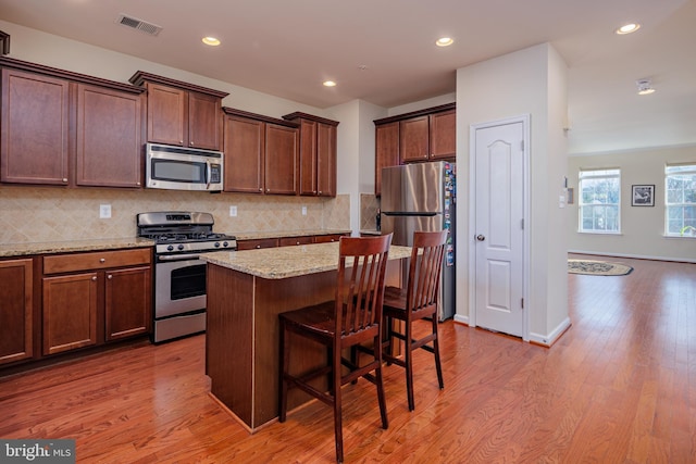 kitchen featuring light hardwood / wood-style floors, appliances with stainless steel finishes, a center island, and light stone counters