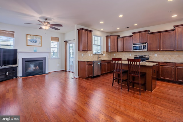 kitchen with hardwood / wood-style flooring, a kitchen island, light stone countertops, appliances with stainless steel finishes, and a breakfast bar area