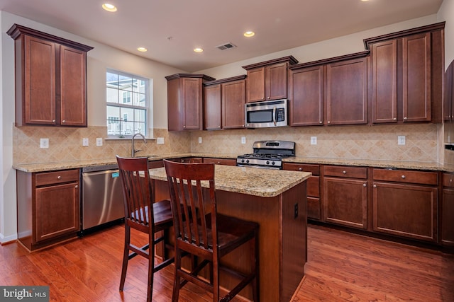 kitchen featuring appliances with stainless steel finishes, dark hardwood / wood-style flooring, light stone countertops, and a center island