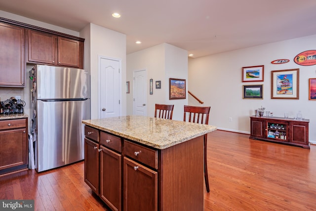 kitchen featuring wood-type flooring, a kitchen island, stainless steel refrigerator, light stone countertops, and a breakfast bar area