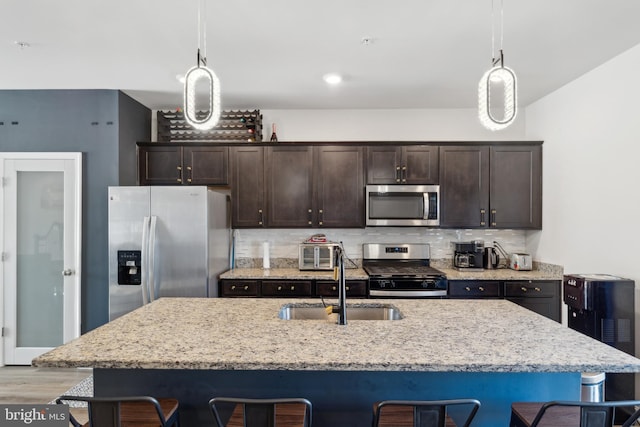 kitchen with sink, a breakfast bar area, decorative light fixtures, an island with sink, and stainless steel appliances