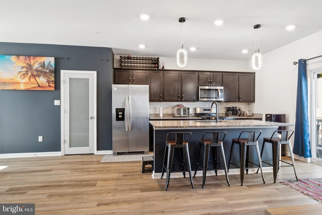 kitchen with stainless steel appliances, an island with sink, hanging light fixtures, and a breakfast bar