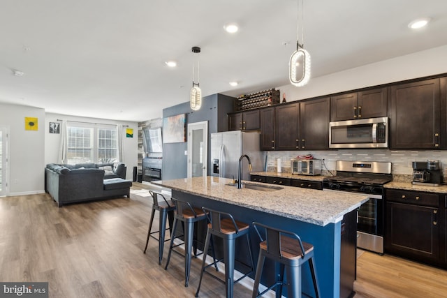 kitchen featuring stainless steel appliances, sink, a center island with sink, and decorative light fixtures