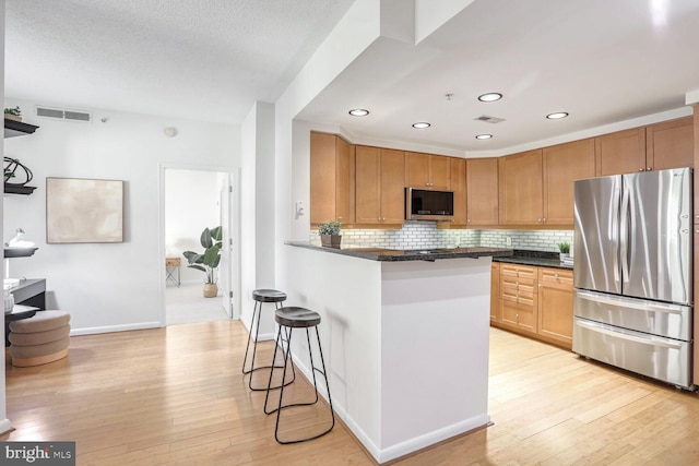 kitchen with appliances with stainless steel finishes, backsplash, a kitchen breakfast bar, light hardwood / wood-style floors, and kitchen peninsula