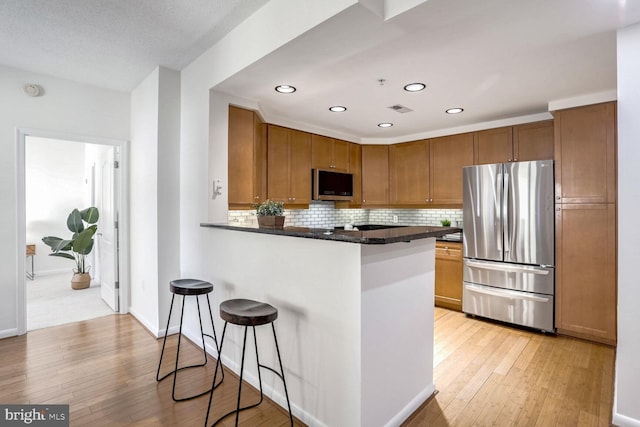 kitchen featuring appliances with stainless steel finishes, dark stone countertops, backsplash, a kitchen breakfast bar, and kitchen peninsula