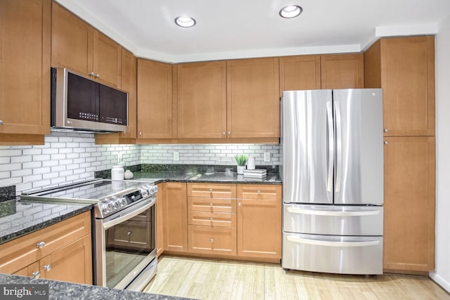 kitchen with stainless steel appliances, light wood-type flooring, decorative backsplash, and dark stone countertops