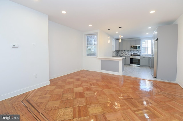 kitchen with gray cabinetry, backsplash, decorative light fixtures, and appliances with stainless steel finishes