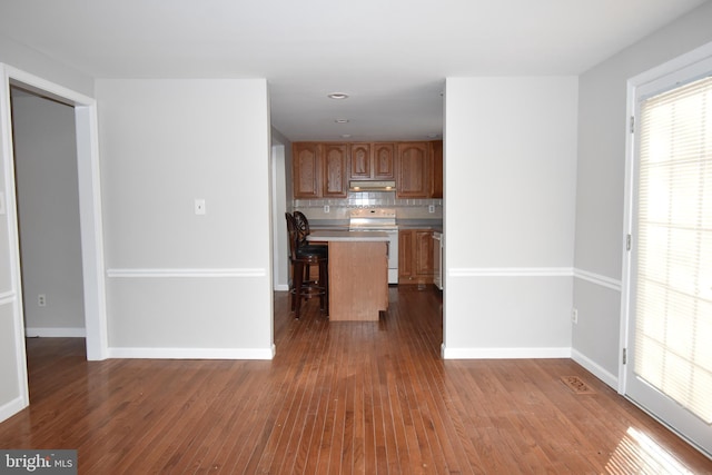 kitchen featuring white electric stove, a kitchen island, a kitchen breakfast bar, light countertops, and under cabinet range hood