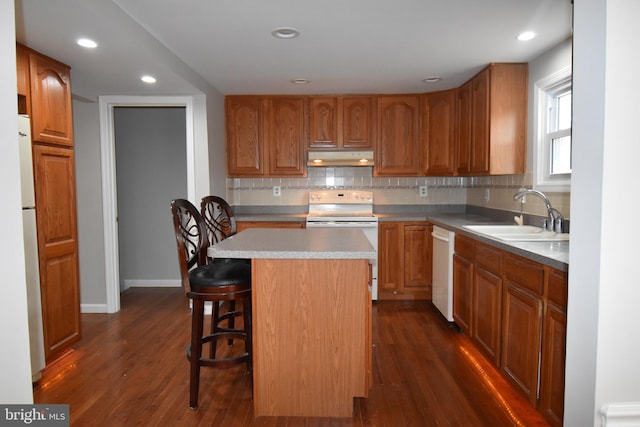 kitchen featuring a breakfast bar area, a kitchen island, a sink, white appliances, and under cabinet range hood