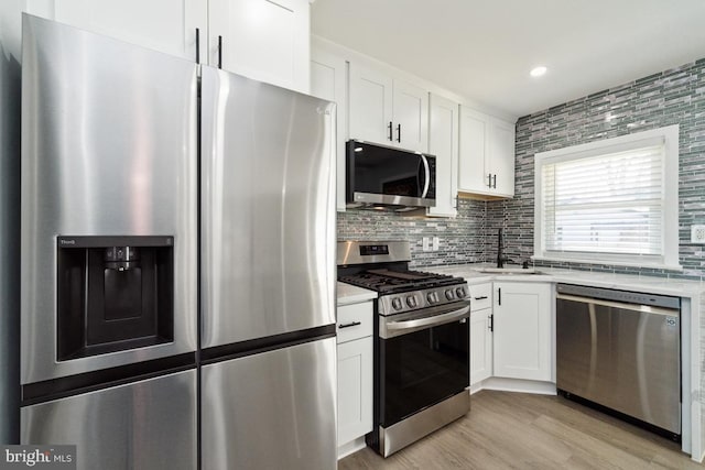 kitchen with sink, white cabinetry, appliances with stainless steel finishes, light hardwood / wood-style floors, and decorative backsplash