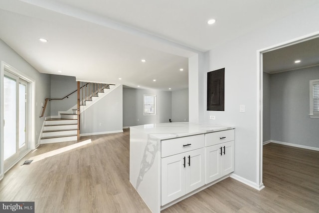 kitchen featuring light stone countertops, light hardwood / wood-style floors, kitchen peninsula, and white cabinets