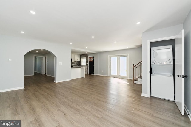 unfurnished living room with stacked washer and clothes dryer and light hardwood / wood-style flooring