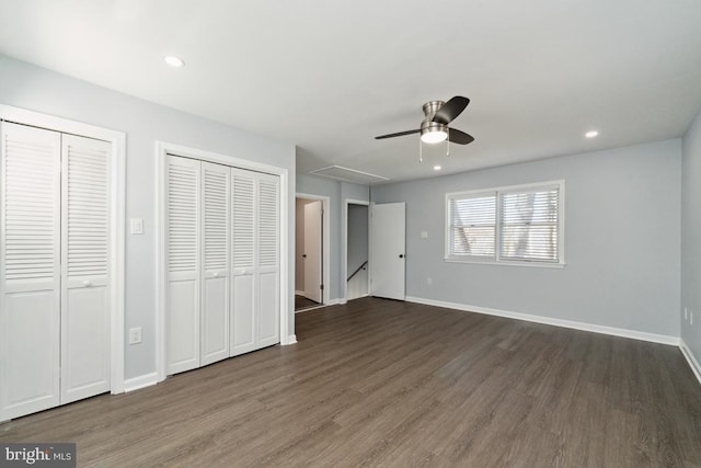 unfurnished bedroom featuring two closets, dark hardwood / wood-style floors, and ceiling fan