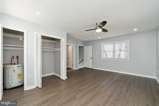 unfurnished bedroom with water heater, dark hardwood / wood-style floors, multiple closets, and ceiling fan