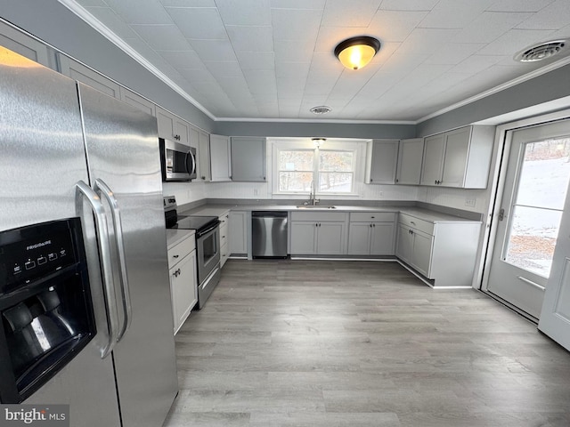 kitchen featuring gray cabinets, sink, ornamental molding, light hardwood / wood-style floors, and stainless steel appliances