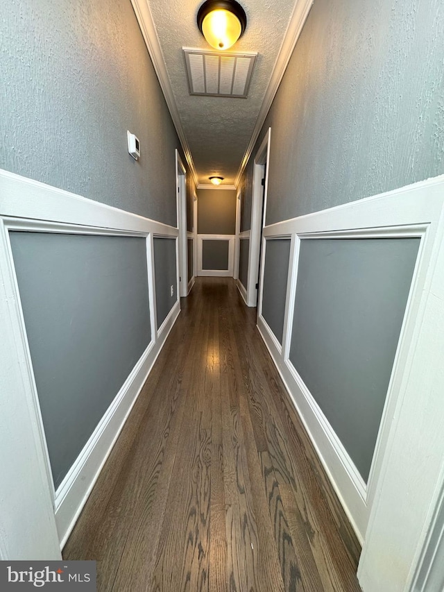 hallway with dark wood-type flooring, ornamental molding, and a textured ceiling