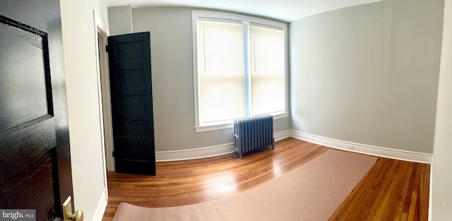 unfurnished room featuring hardwood / wood-style floors, a healthy amount of sunlight, and radiator heating unit