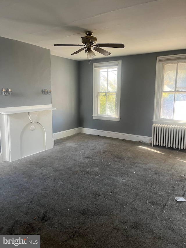 unfurnished living room with radiator, a wealth of natural light, and carpet flooring