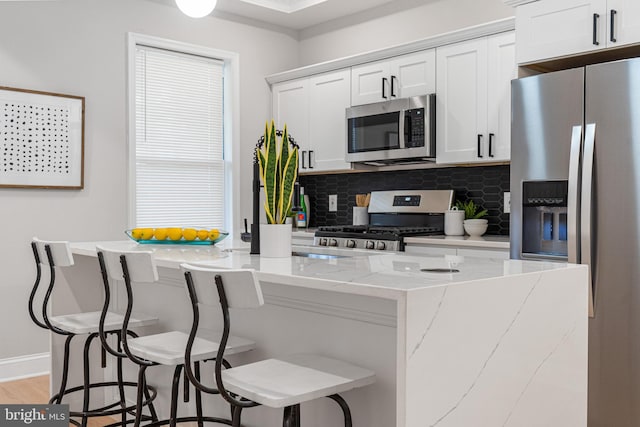 kitchen with light stone countertops, backsplash, stainless steel appliances, and white cabinets