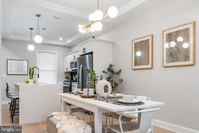 dining space with sink, light hardwood / wood-style flooring, ornamental molding, and a raised ceiling