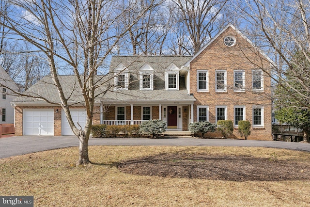 view of front of property with aphalt driveway, an attached garage, covered porch, brick siding, and a front lawn