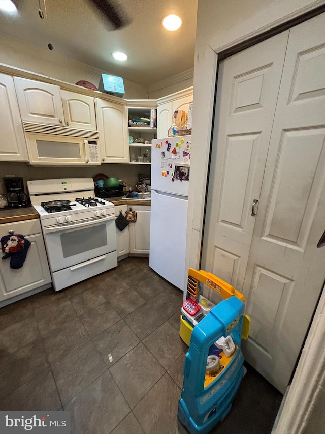 kitchen with white cabinetry, dark tile patterned flooring, and white appliances