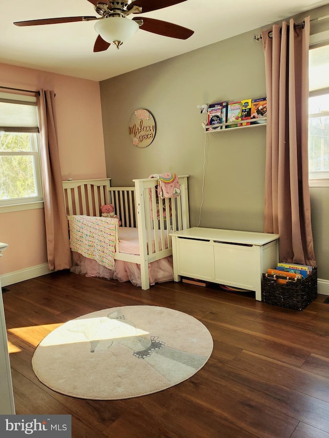 unfurnished bedroom featuring multiple windows, dark hardwood / wood-style flooring, a nursery area, and ceiling fan