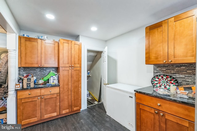 kitchen featuring fridge, dark stone counters, dark hardwood / wood-style flooring, and tasteful backsplash