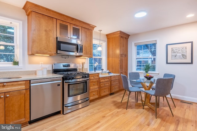 kitchen with brown cabinets, stainless steel appliances, a wealth of natural light, visible vents, and light wood-style flooring