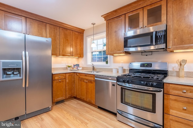 kitchen featuring appliances with stainless steel finishes, light wood-type flooring, a sink, and brown cabinets