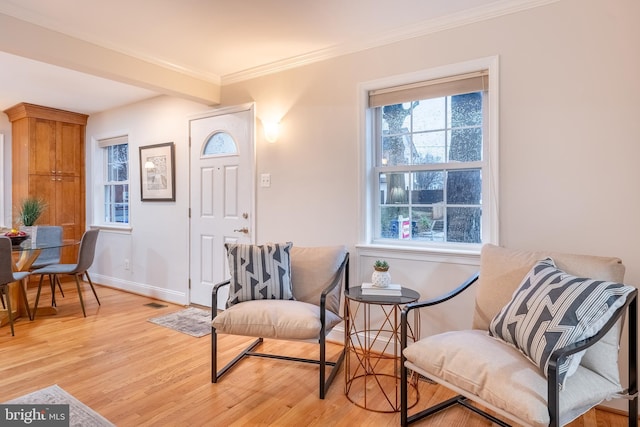 living area featuring light wood finished floors, visible vents, baseboards, and ornamental molding