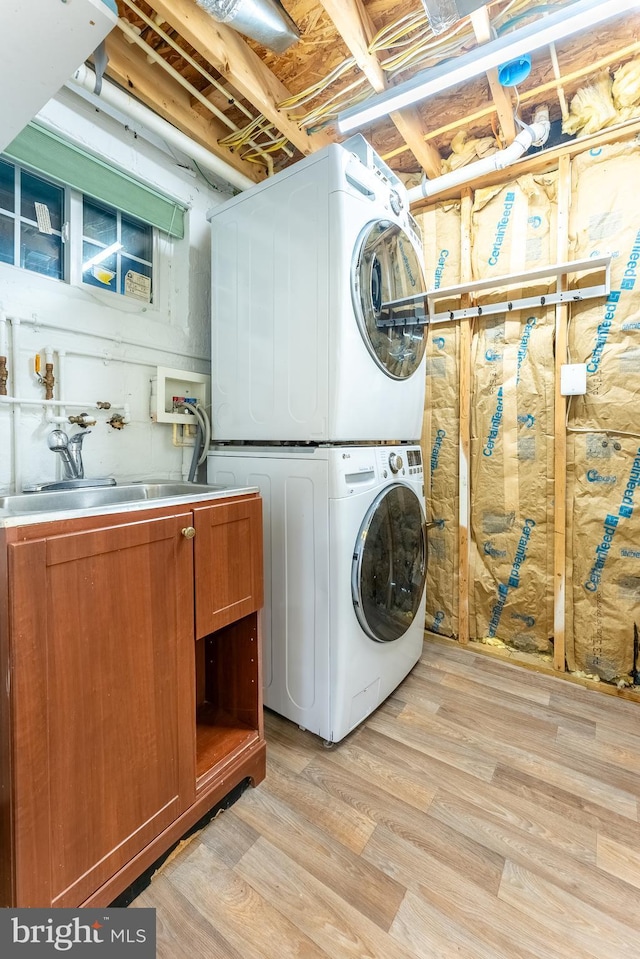 clothes washing area with stacked washer / dryer, light wood-type flooring, a sink, and cabinet space