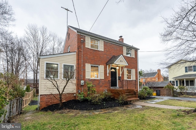 view of front of property with brick siding, a chimney, a front yard, and fence