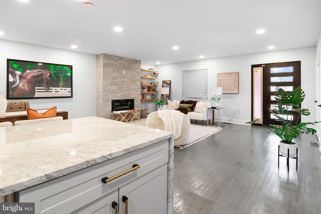 kitchen with a tiled fireplace, white cabinetry, dark wood-type flooring, and light stone counters