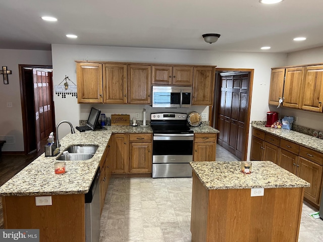 kitchen with light stone counters, stainless steel appliances, sink, and a center island with sink