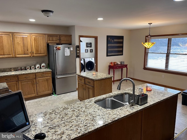 kitchen with sink, washing machine and dryer, stainless steel refrigerator, light stone countertops, and a kitchen island with sink