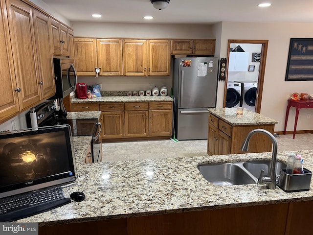 kitchen featuring sink, a center island, washer and dryer, appliances with stainless steel finishes, and light stone countertops