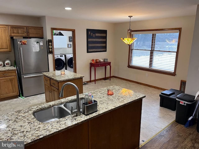 kitchen with sink, light stone counters, separate washer and dryer, stainless steel refrigerator, and a kitchen island