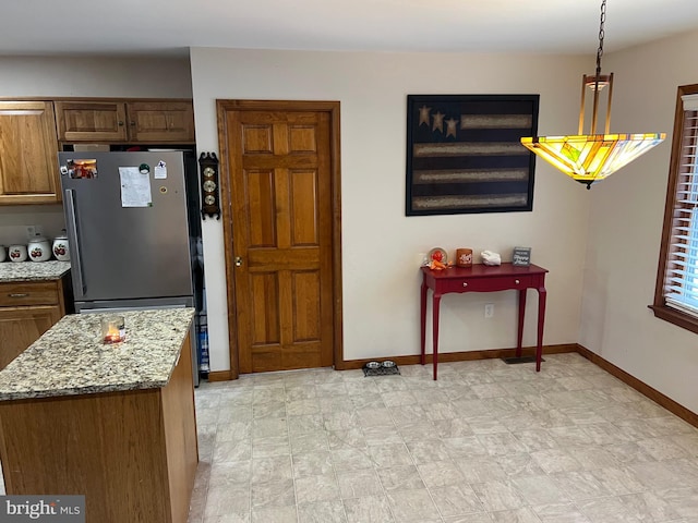 kitchen featuring stainless steel refrigerator, decorative light fixtures, and light stone countertops