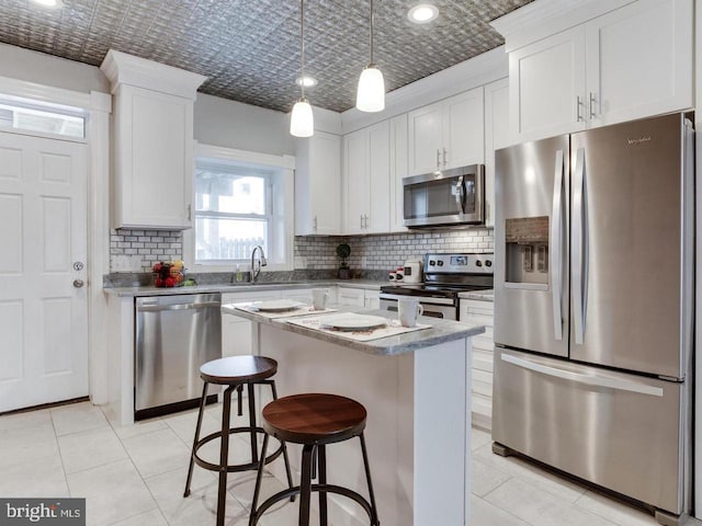 kitchen with a center island, hanging light fixtures, appliances with stainless steel finishes, decorative backsplash, and white cabinets