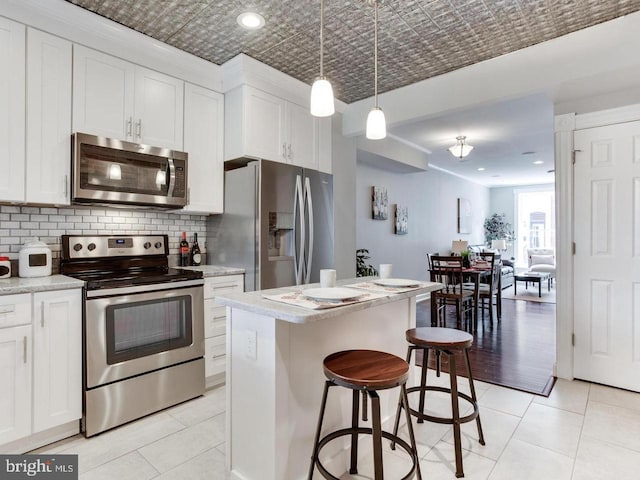 kitchen with appliances with stainless steel finishes, white cabinetry, hanging light fixtures, backsplash, and a kitchen island