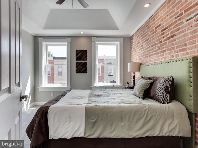 carpeted bedroom with brick wall, ceiling fan, and a tray ceiling