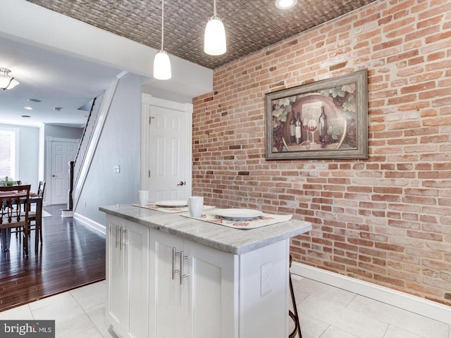 kitchen with pendant lighting, light stone countertops, white cabinets, and brick wall