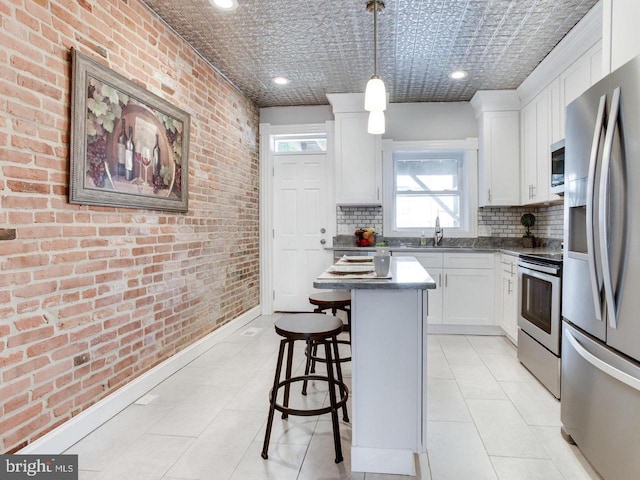 kitchen featuring a kitchen island, brick wall, appliances with stainless steel finishes, pendant lighting, and white cabinets