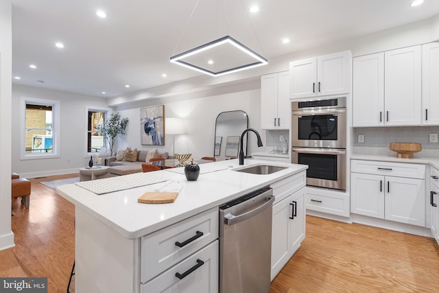 kitchen featuring appliances with stainless steel finishes, white cabinetry, sink, a kitchen island with sink, and light hardwood / wood-style flooring