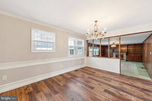 empty room featuring hardwood / wood-style flooring, a notable chandelier, ornamental molding, brick wall, and a brick fireplace