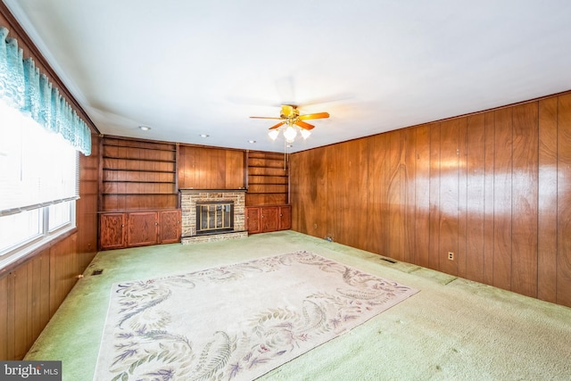 unfurnished living room with light colored carpet, built in features, a fireplace, and wood walls